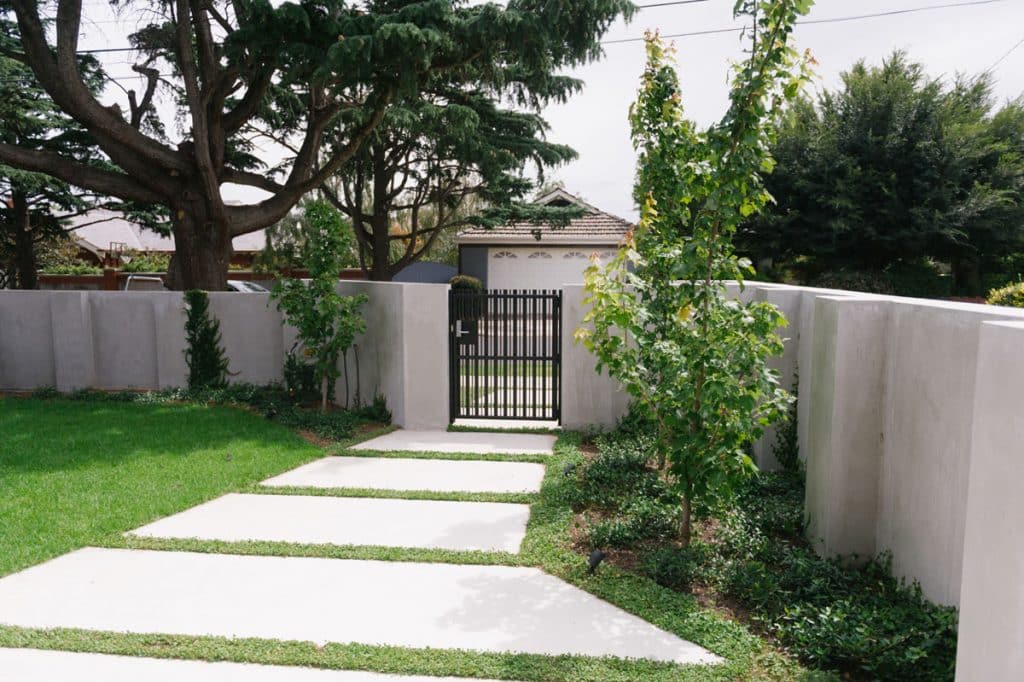 behind a gated concrete front entrance with lawn and custom designed pavers