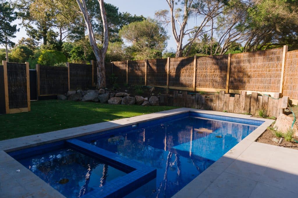 wicker fence and custom retaining wall behind a concrete courtyard pool and spa