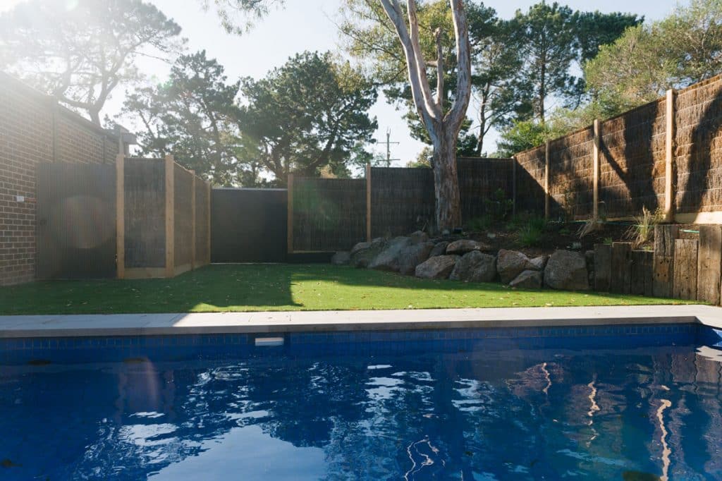 inside a custom courtyard pool with wicker fencing and rock retaining wall